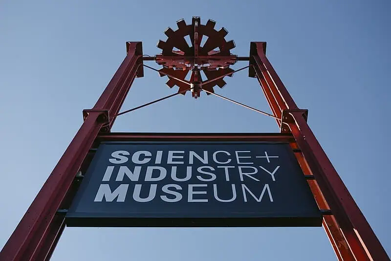 Signage of the Science and Industry Museum in Manchester, featuring a red gear design against a clear blue sky